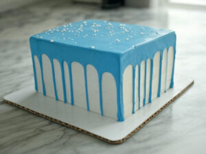 Rectangular blue gender reveal cake with a drip effect and tiny edible stars, placed on a marble countertop